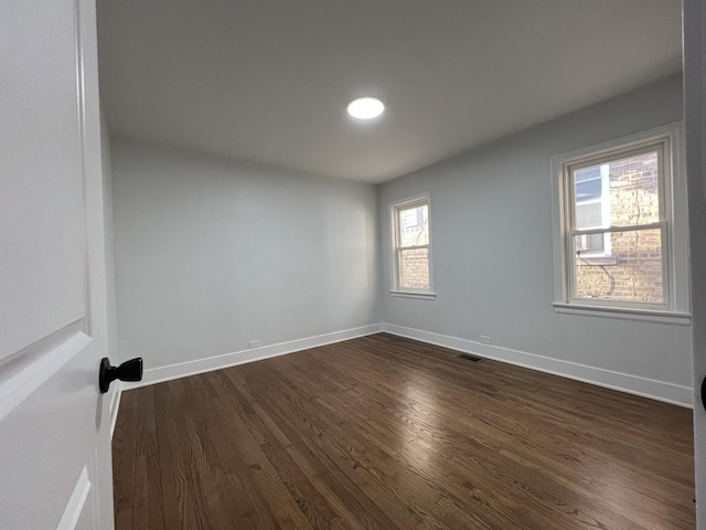 spare room with visible vents, baseboards, and dark wood-type flooring