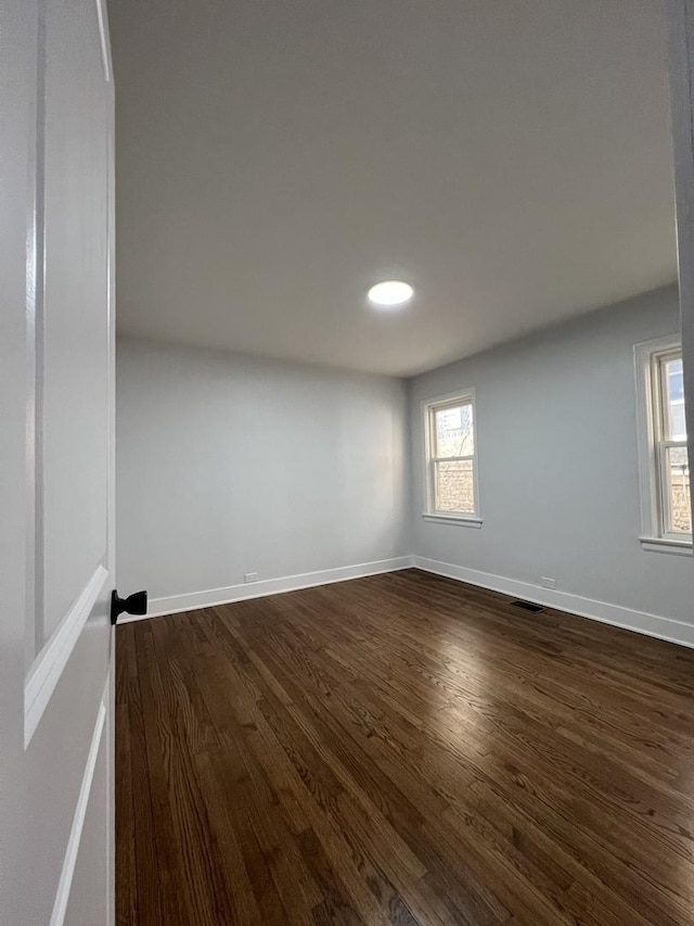 spare room featuring visible vents, dark wood-style floors, and baseboards