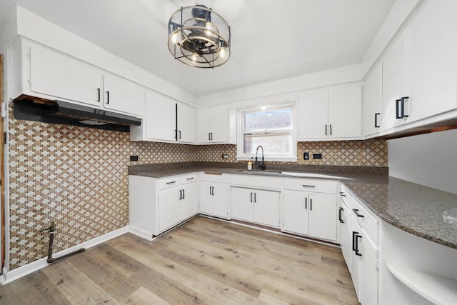 kitchen with a sink, under cabinet range hood, tasteful backsplash, white cabinets, and light wood finished floors