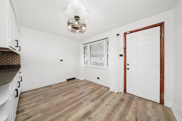 unfurnished dining area featuring a notable chandelier, baseboards, and light wood-style floors