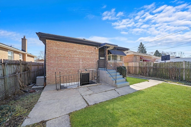 back of property with brick siding, central air condition unit, a lawn, and a fenced backyard