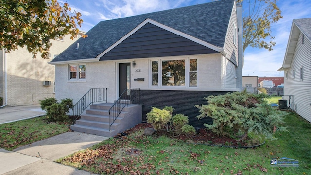 view of front of house with brick siding, a front lawn, and roof with shingles