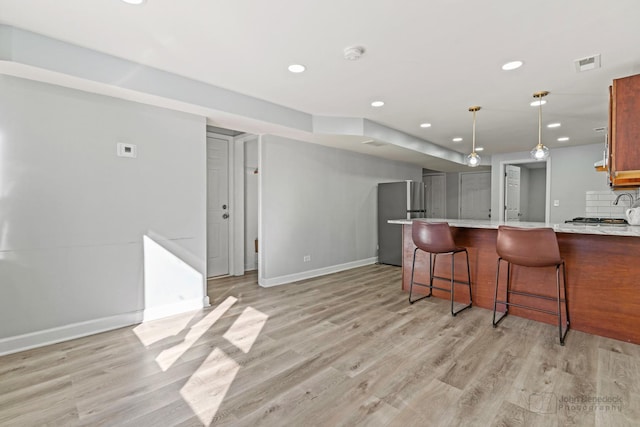 kitchen featuring visible vents, baseboards, freestanding refrigerator, decorative backsplash, and light wood-style floors