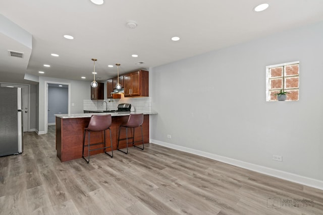 kitchen featuring visible vents, freestanding refrigerator, a peninsula, light countertops, and decorative backsplash