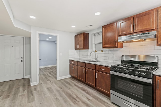 kitchen with stainless steel gas range, light wood-style flooring, a sink, under cabinet range hood, and backsplash