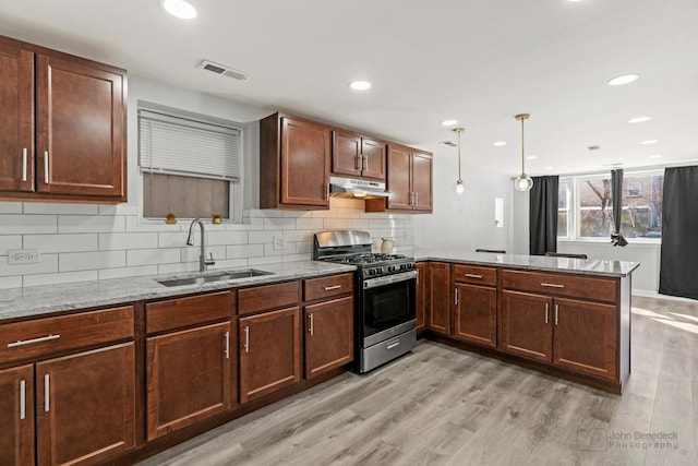 kitchen featuring visible vents, stainless steel range with gas cooktop, under cabinet range hood, a peninsula, and a sink