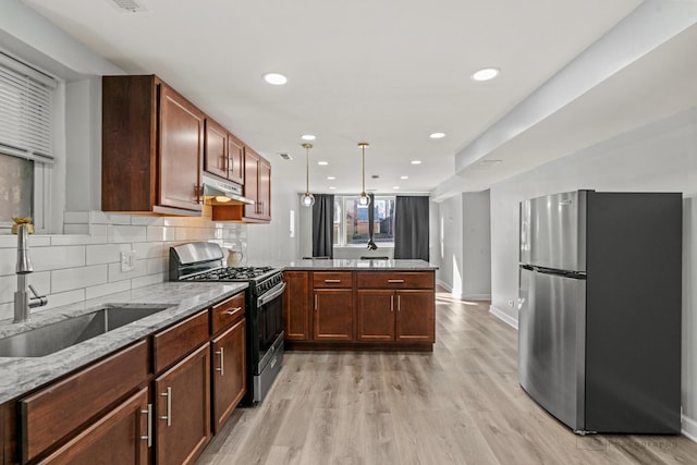 kitchen with under cabinet range hood, a sink, gas range oven, freestanding refrigerator, and a peninsula