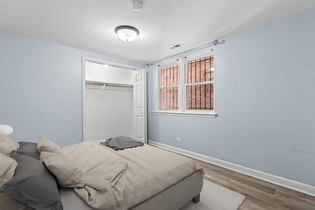 bedroom with a closet, baseboards, visible vents, and wood finished floors