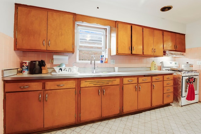 kitchen with brown cabinetry, light floors, a sink, light countertops, and white gas range