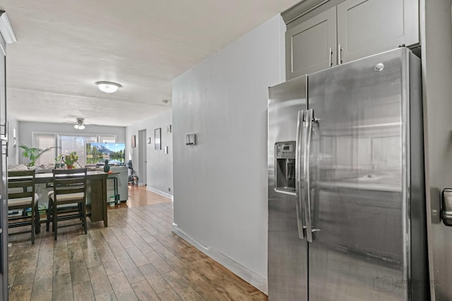 kitchen featuring ceiling fan, baseboards, wood finished floors, and stainless steel refrigerator with ice dispenser