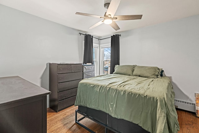 bedroom featuring ceiling fan, a baseboard heating unit, and wood finished floors