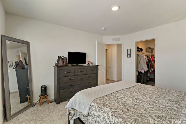 bedroom with visible vents, baseboards, light colored carpet, and a spacious closet