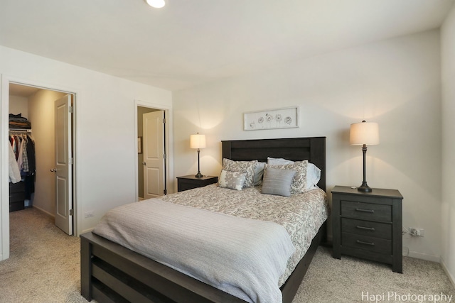 bedroom with a spacious closet, baseboards, a closet, and light carpet