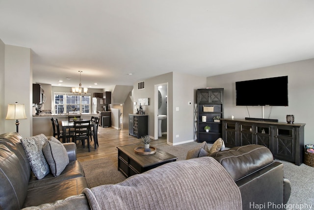 living area with light wood-type flooring, visible vents, baseboards, and a chandelier