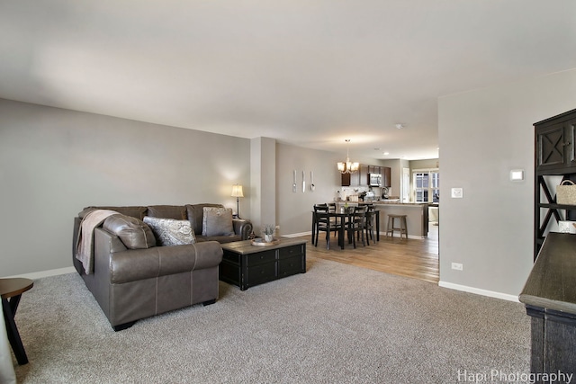 living room featuring baseboards, light carpet, and a notable chandelier