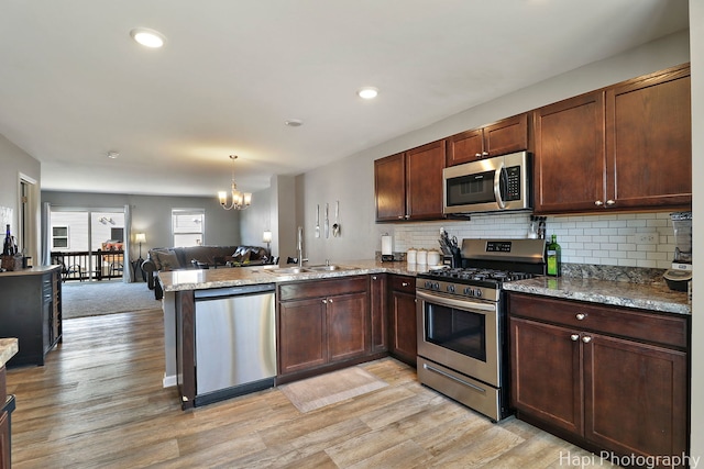 kitchen featuring light wood finished floors, open floor plan, a peninsula, stainless steel appliances, and a sink