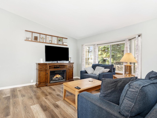 living area with light wood finished floors, a warm lit fireplace, baseboards, and vaulted ceiling