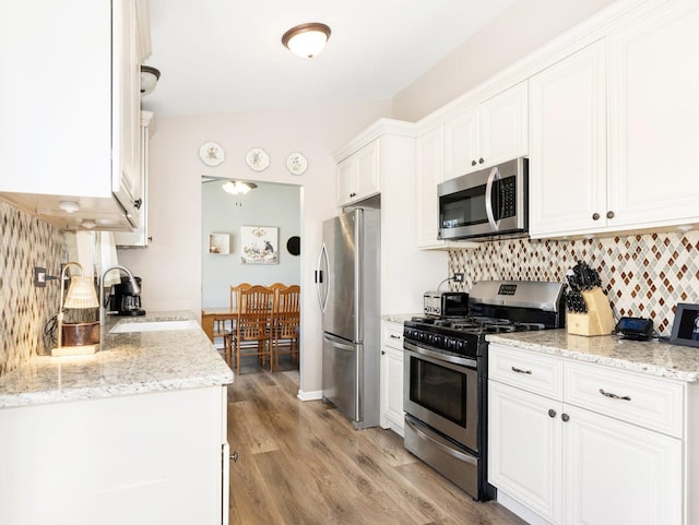 kitchen featuring light wood-style flooring, a sink, tasteful backsplash, stainless steel appliances, and white cabinets