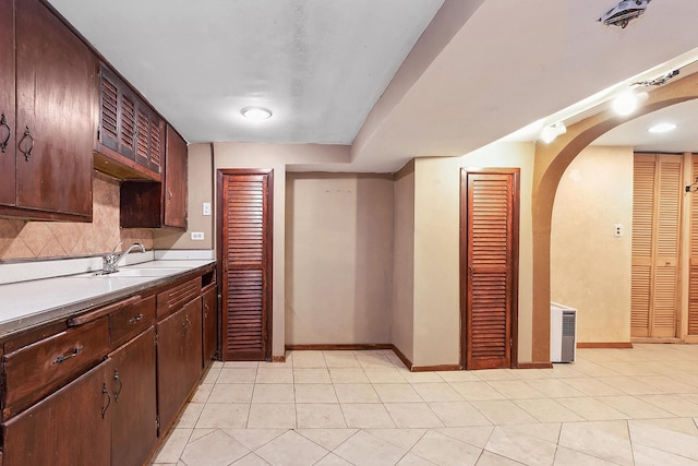 kitchen featuring baseboards, arched walkways, a sink, light countertops, and tasteful backsplash