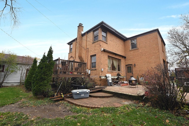 rear view of house featuring a wooden deck, brick siding, a chimney, and a patio area