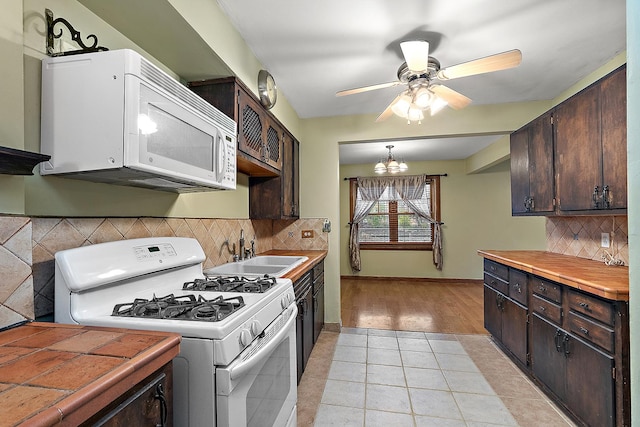 kitchen featuring ceiling fan with notable chandelier, a sink, white appliances, light tile patterned floors, and dark brown cabinets