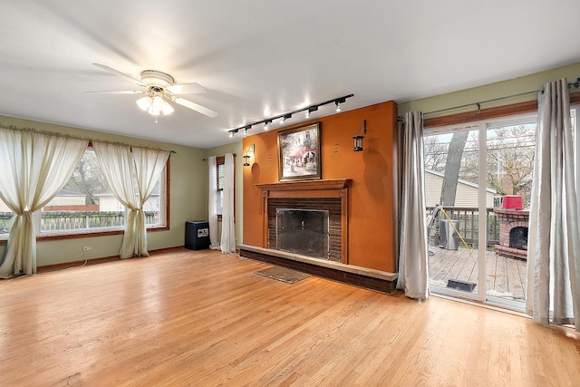 unfurnished living room with a brick fireplace, wood finished floors, a ceiling fan, and a healthy amount of sunlight