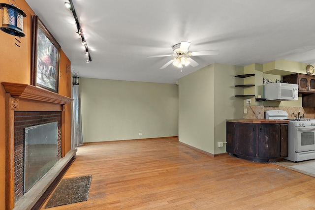 living room with baseboards, a brick fireplace, ceiling fan, and light wood finished floors