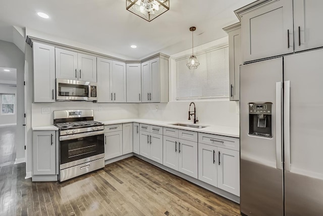 kitchen with wood finished floors, a sink, stainless steel appliances, light countertops, and decorative light fixtures