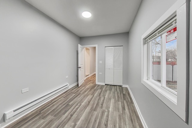 unfurnished bedroom with a closet, baseboard heating, baseboards, and wood finished floors