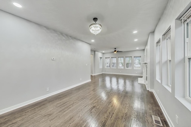 unfurnished living room featuring visible vents, ceiling fan with notable chandelier, dark wood finished floors, recessed lighting, and baseboards