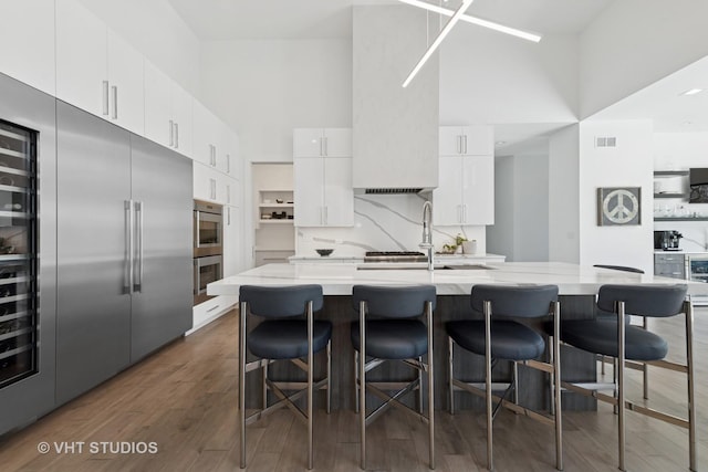 kitchen featuring visible vents, a sink, white cabinetry, a towering ceiling, and stainless steel appliances