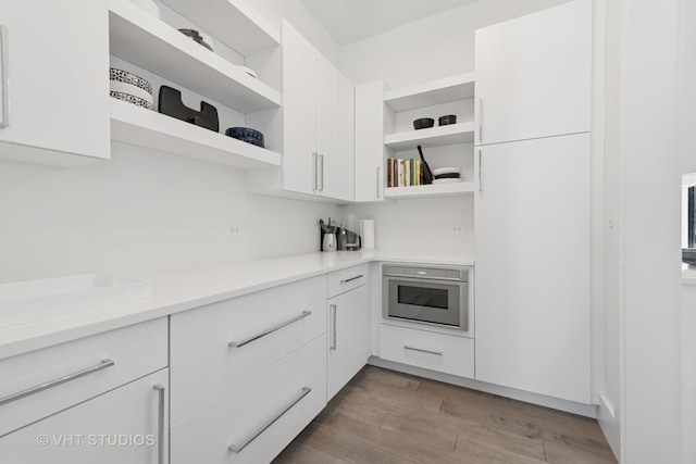 kitchen with white cabinetry, oven, open shelves, and wood finished floors