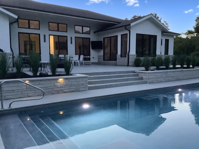 rear view of property featuring a patio, an outdoor pool, and stucco siding