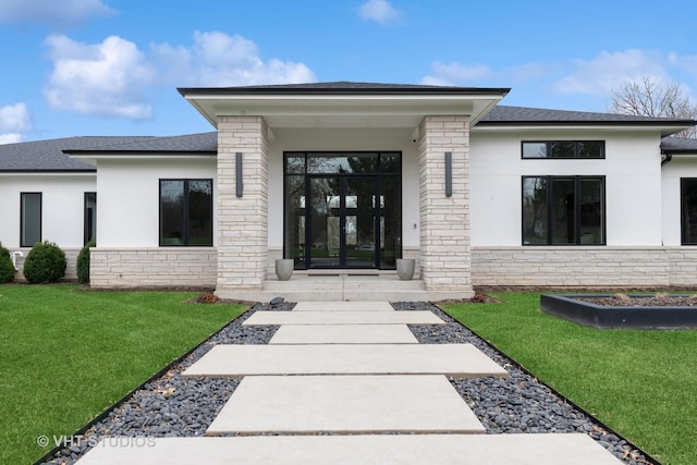 property entrance featuring roof with shingles, a yard, stucco siding, and stone siding