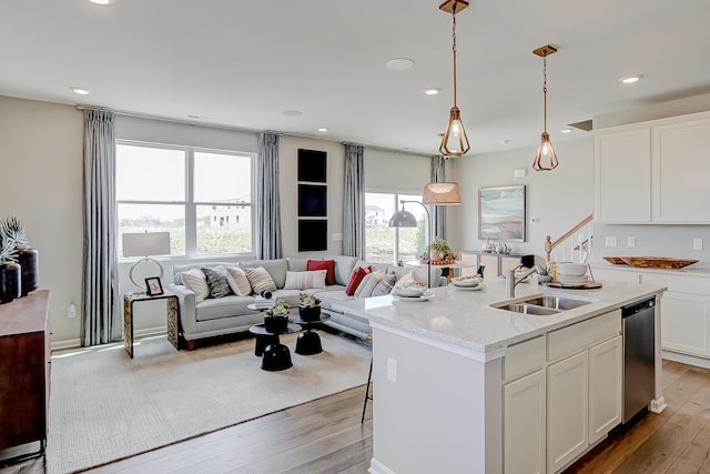 kitchen featuring white cabinetry, a sink, wood-type flooring, stainless steel dishwasher, and open floor plan