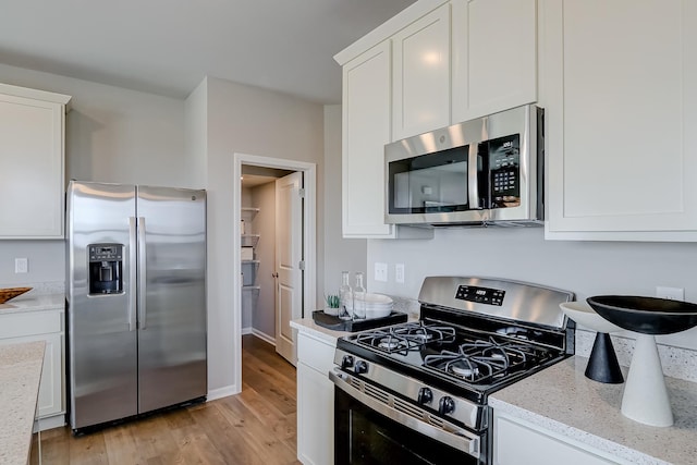 kitchen with white cabinets, appliances with stainless steel finishes, light wood-style floors, and light stone countertops