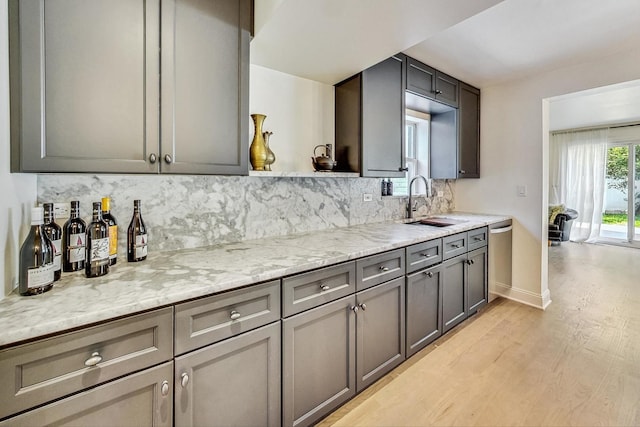 kitchen featuring backsplash, gray cabinetry, dishwasher, light wood-style floors, and a sink