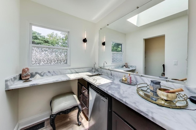 bathroom with visible vents, a sink, wood finished floors, a skylight, and baseboards