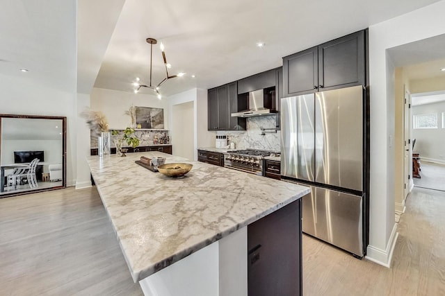 kitchen featuring light stone counters, tasteful backsplash, light wood-style floors, appliances with stainless steel finishes, and wall chimney exhaust hood