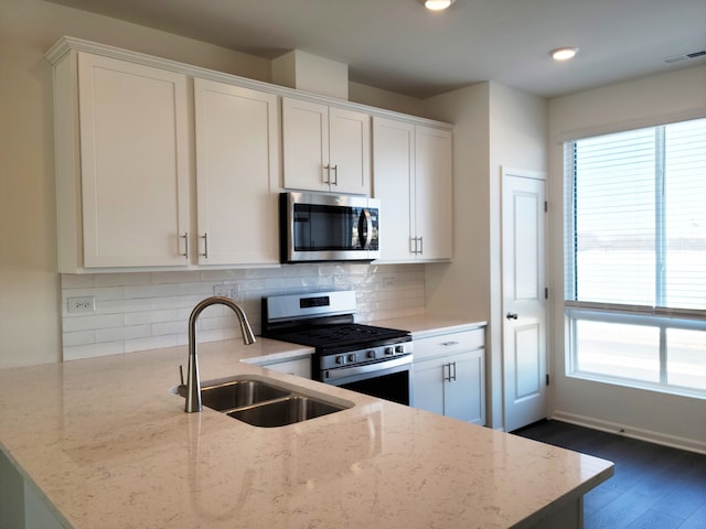 kitchen with light stone counters, a sink, decorative backsplash, stainless steel appliances, and white cabinets