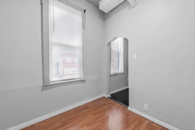 unfurnished room with wood finished floors, baseboards, and arched walkways