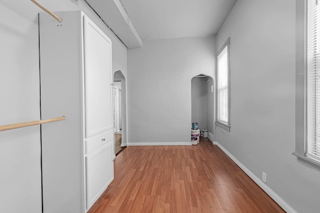 interior space featuring baseboards, arched walkways, and light wood finished floors