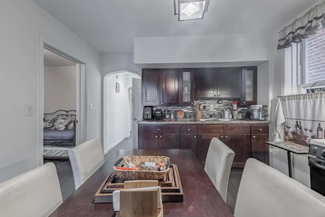 kitchen featuring backsplash, glass insert cabinets, dark brown cabinetry, light countertops, and arched walkways