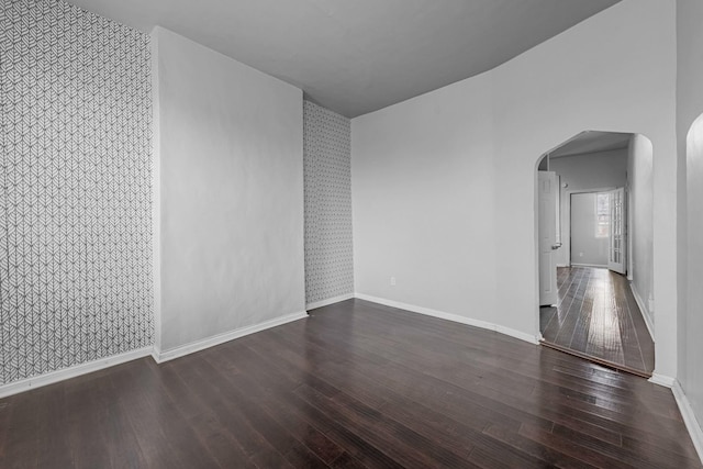 unfurnished room featuring arched walkways, dark wood-type flooring, and baseboards