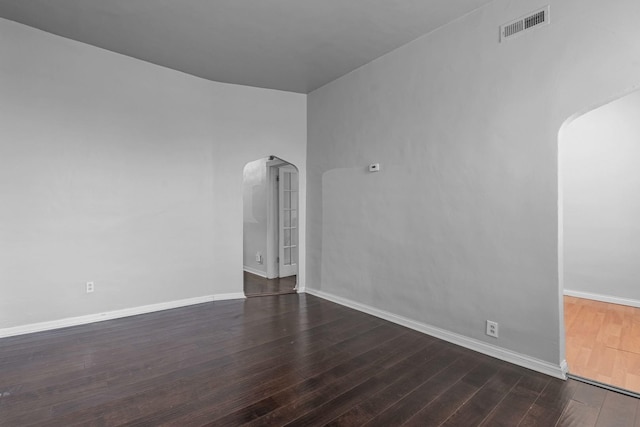 spare room with visible vents, arched walkways, baseboards, and wood-type flooring