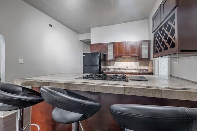 kitchen featuring black appliances, a kitchen breakfast bar, glass insert cabinets, and backsplash