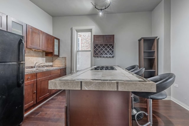 kitchen featuring a breakfast bar, dark wood finished floors, a sink, decorative backsplash, and black appliances