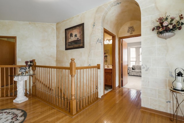 hallway featuring an upstairs landing, arched walkways, and hardwood / wood-style flooring