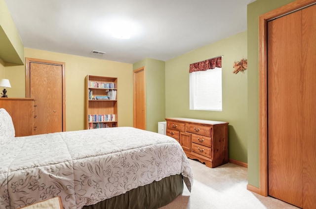 bedroom with light carpet, visible vents, two closets, and baseboards