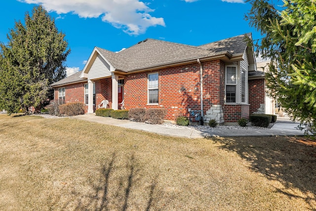 view of side of home featuring brick siding, stone siding, a yard, and roof with shingles